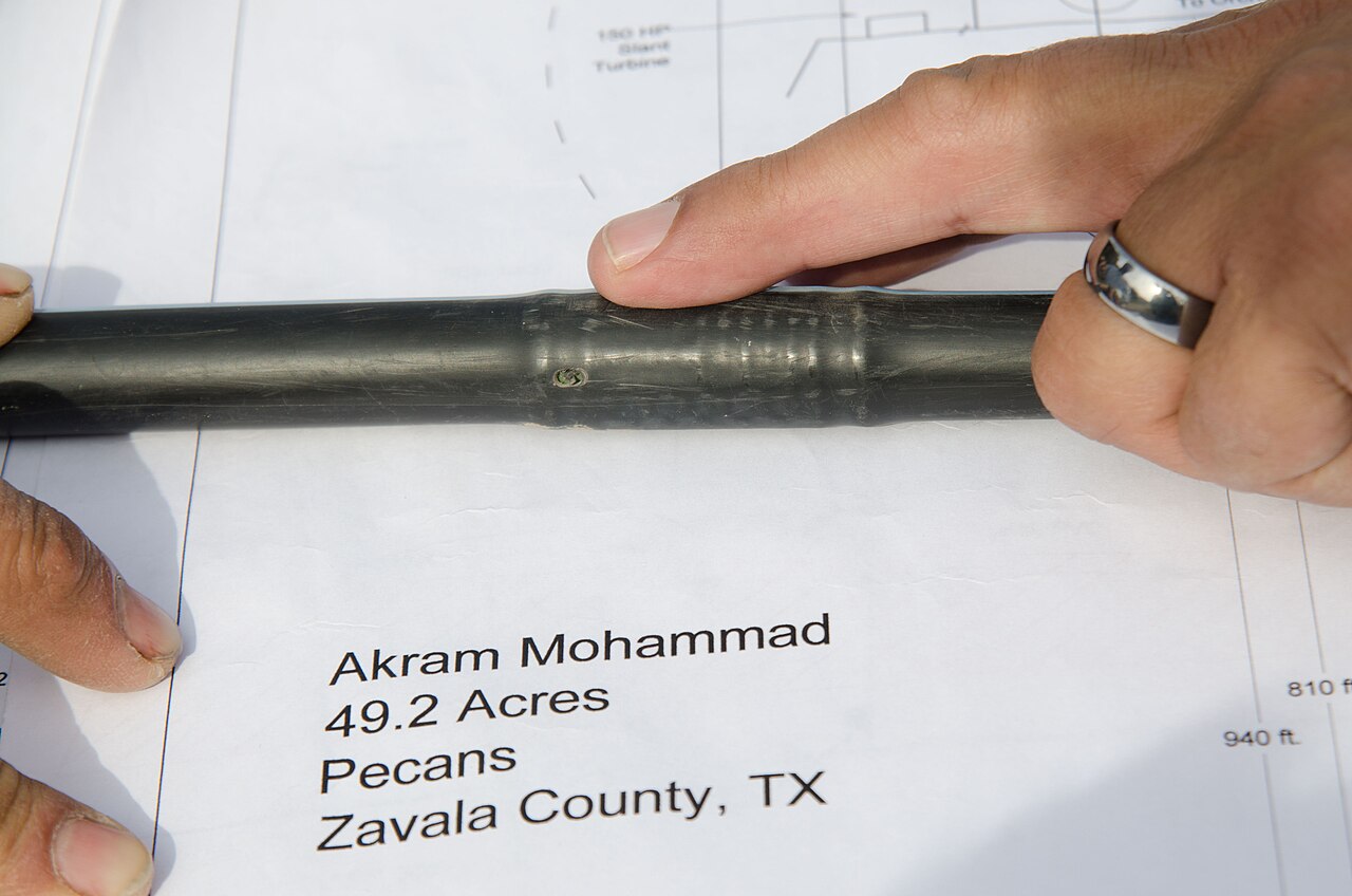 Hands holding irrigation tubing and an emitter above a farm plan.