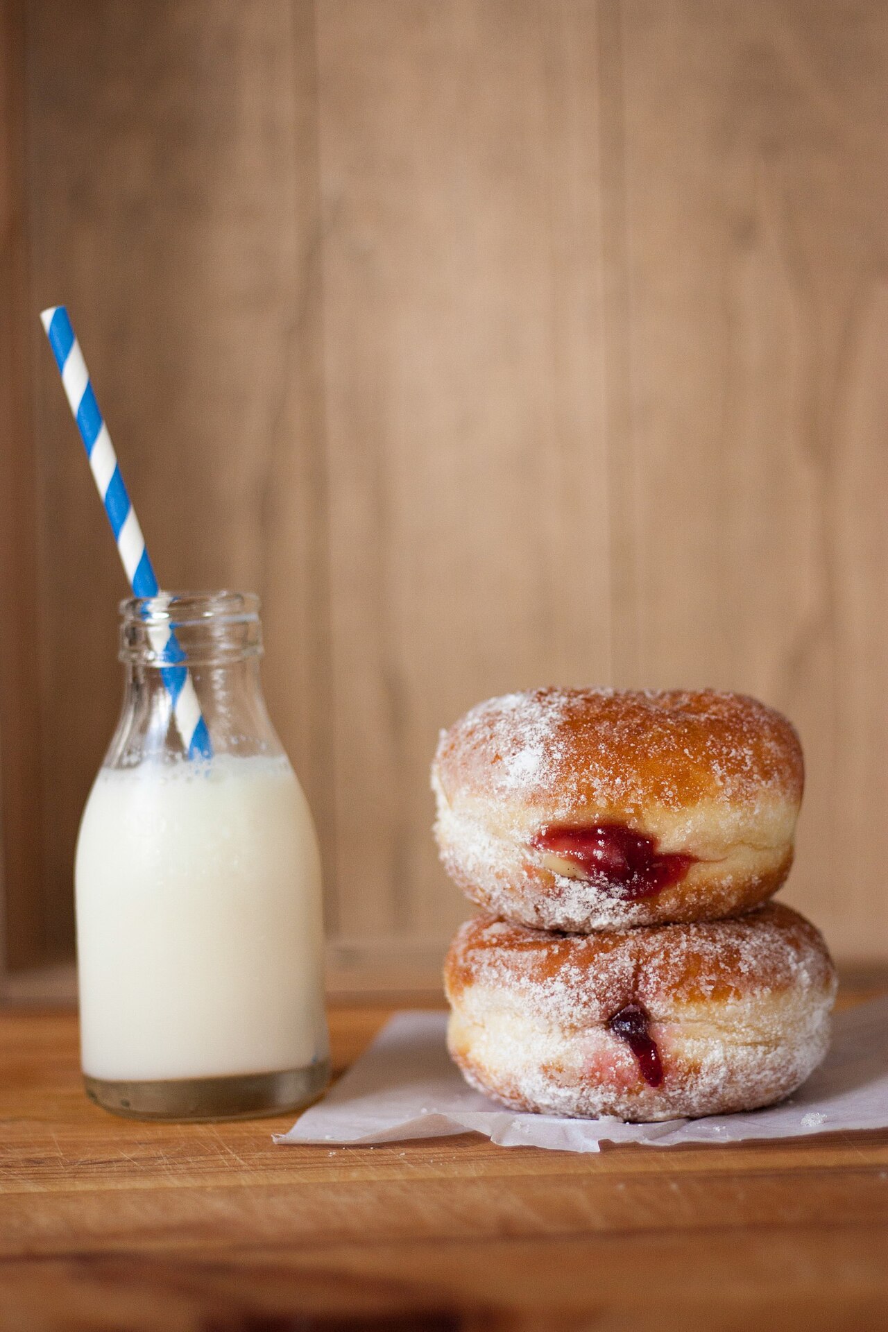 A glass bottle of milk beside two doughnuts.