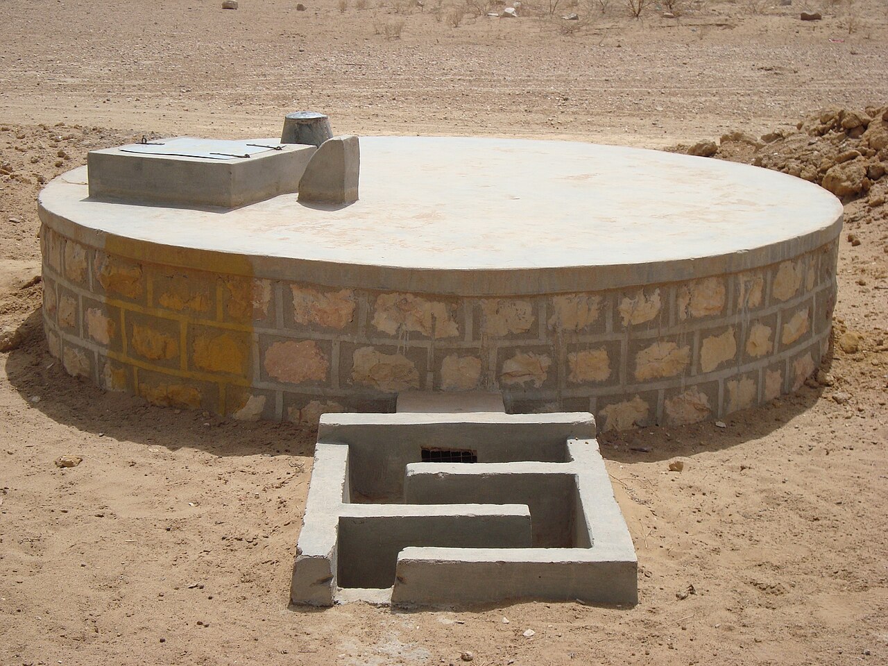 A circular covered masonry water tank with access steps.