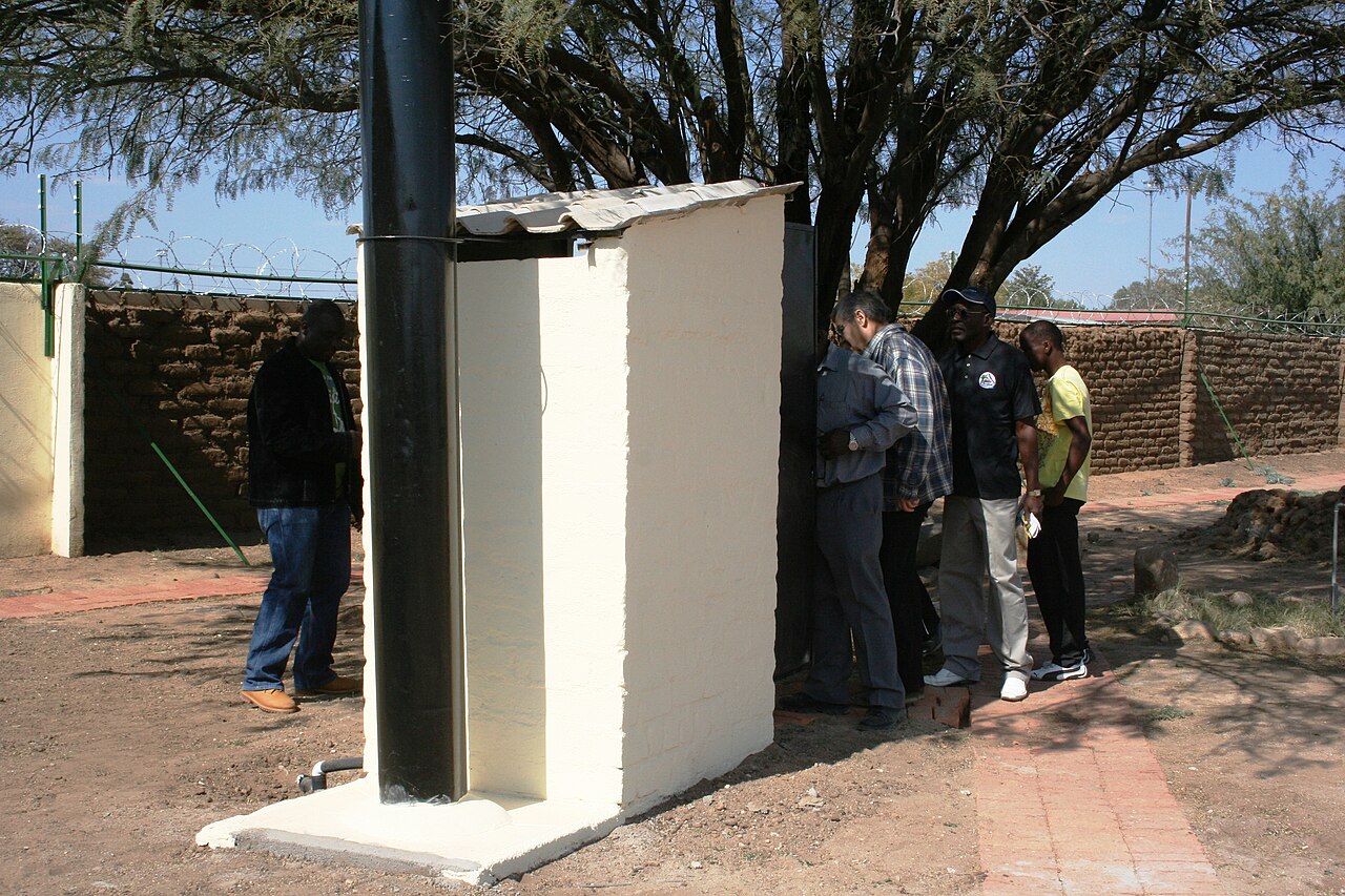 Otji toilet building with a ventilation pipe and people nearby